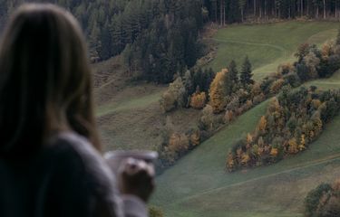 Donna con tazza in mano ammira i prati e i boschi autunnali in Valle Aurina, Alto Adige